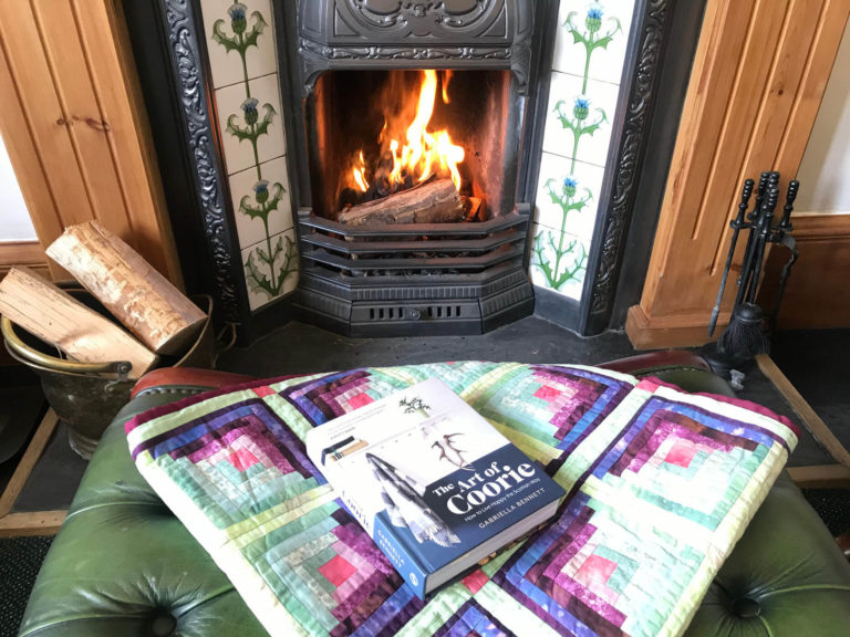 The Art of Coorie book in front of the open fire in Fern Villa Ballachulish Guest Lounge
